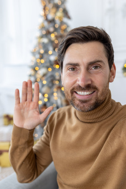 垂直特写照片，一个年轻人在家里对着摄像机打视频电话，挥手并祝愿新年和圣诞节快乐图片下载