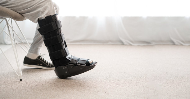 腿上装着黑色夹板的受伤男子坐在椅子上。踝足矫形器图片下载