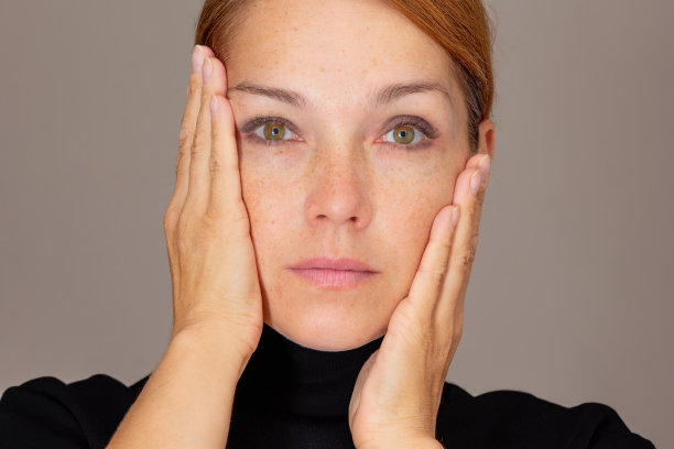 照片中的女人看着相机，手掌放在脸颊上，惊讶于柔软的皮肤图片下载