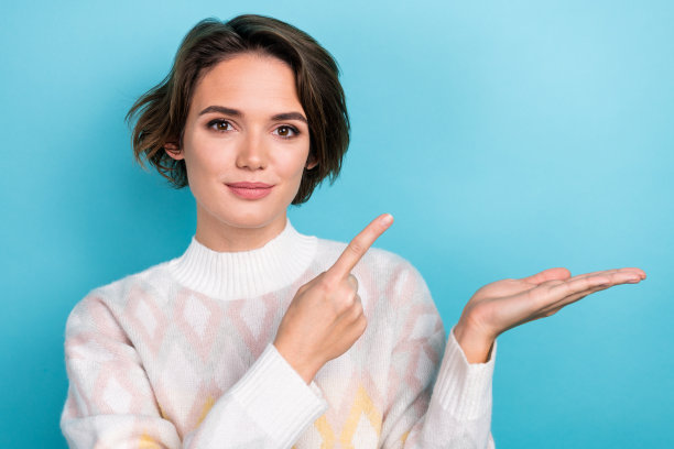 满意的年轻女士的照片，时尚的衣服，温暖的毛衣，指示手指手掌拿轻产品孤立在蓝色背景图片下载