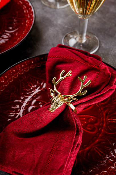 圣诞餐桌设置，餐巾与金戒指鹿在红色盘子近距离垂直照片图片下载