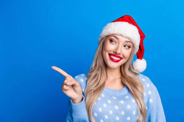 迷人的金发女郎的照片肖像点看空空间穿着毛衣圣诞帽孤立的蓝色背景图片下载