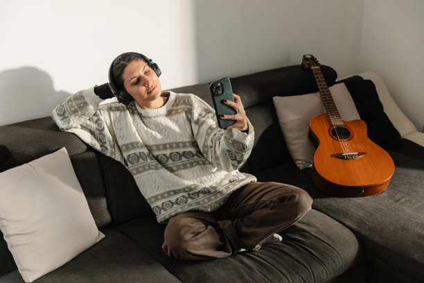 拍摄的一个年轻女子放松在沙发上，听音乐在她的智能手机-股票照片图片下载