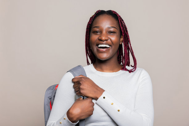 一个开朗的非洲裔年轻女子，扎着辫子，穿着休闲服，肩上背着背包，微笑着指着自己，兴奋地准备学习图片下载