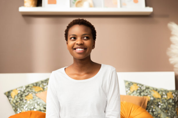 这张照片上，一个爱做梦的非洲裔黑皮肤年轻女子，周末坐在家里的床上放松，休息一天图片下载