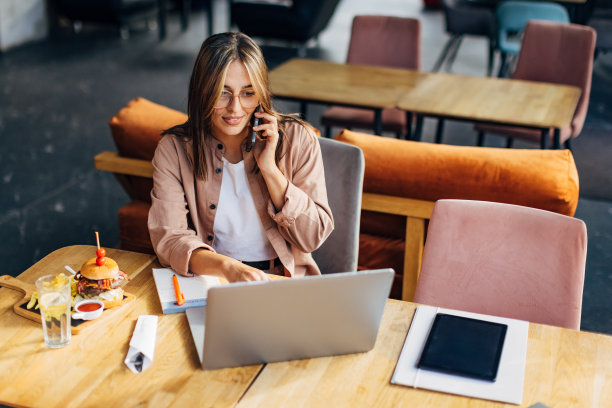 一位女士坐在餐厅里打电话，同时看着笔记本电脑的屏幕图片下载