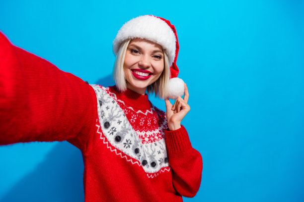 漂亮迷人的圣诞老人帮手的照片穿着装饰毛衣录制视频视频博客孤立的蓝色背景图片下载