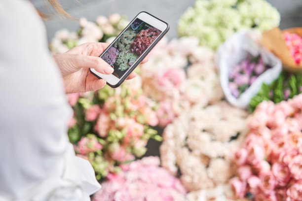 一位女士用手机拍了一张花的照片。花店概念。花店女在柳条篮子里插花。花交付。一个女人写视频博客或在线课程图片下载