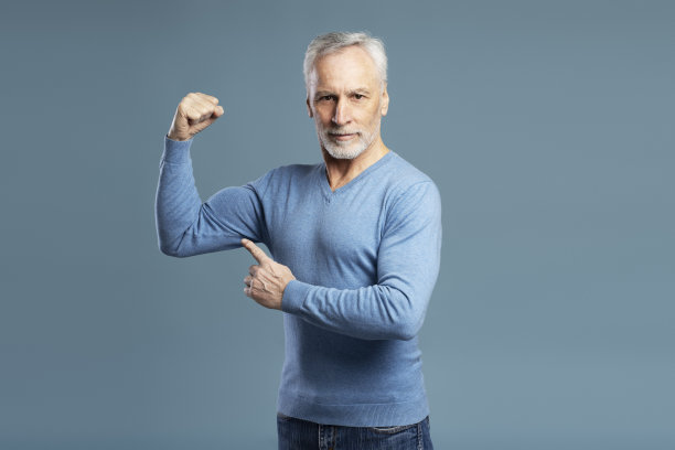 在蓝色背景下，一个强壮的老人看着镜头，露出肌肉。健身房锻炼，运动图片下载