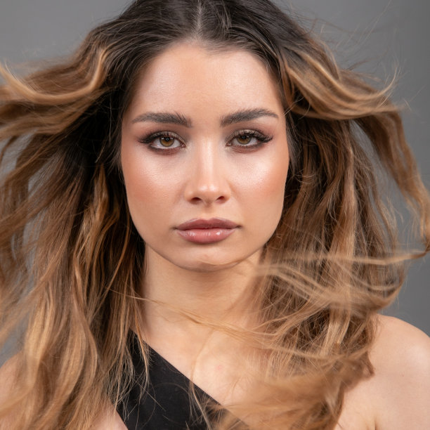 照片美丽的女性脸与飘动的头发特写，看着相机在灰色背景的工作室。图片下载