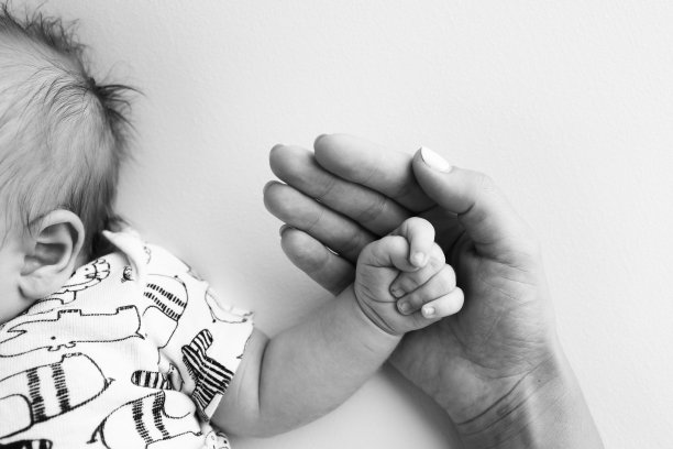 父母的手握着新生婴儿的手指。一对父母的手握着一个新生婴儿的拳头(特写)。家庭保健和医疗保健。黑白照片里小小的手指。图片下载