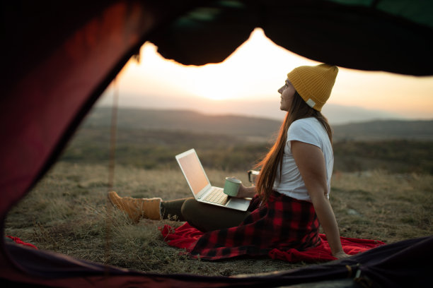 日出时帐篷里的女人在用笔记本电脑。库存图片图片下载