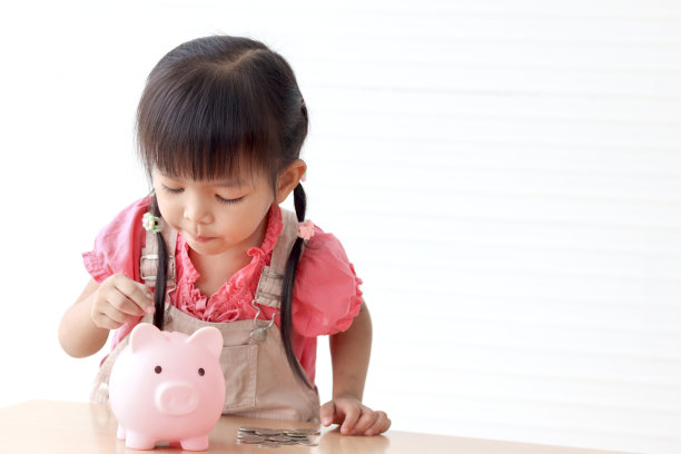 快乐微笑的亚洲小女孩，粉红色的扑满放在桌子上，孩子需要在扑满里收集硬币，收集钱，为未来理财储蓄或投资的概念。图片下载