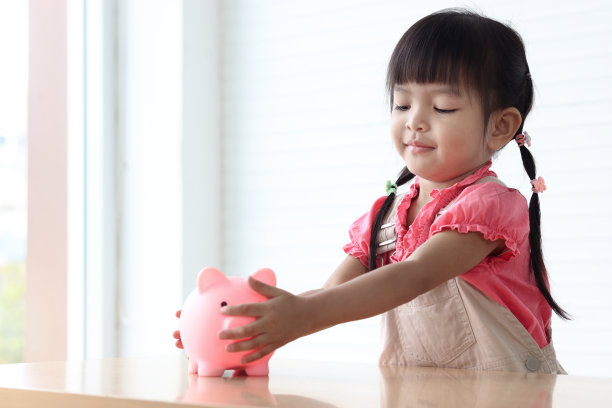 快乐微笑的亚洲小女孩，粉红色的扑满放在桌子上，孩子需要在扑满里收集硬币，收集钱，为未来理财储蓄或投资的概念。图片下载