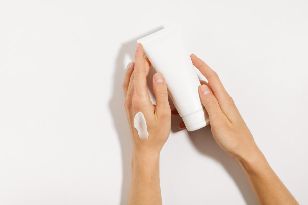 涂抹了润肤霜的女性手拿着白色的面部或身体霜模型管，在白色的孤立背景上。概念护肤、美容产品。图片为您的设计图片下载