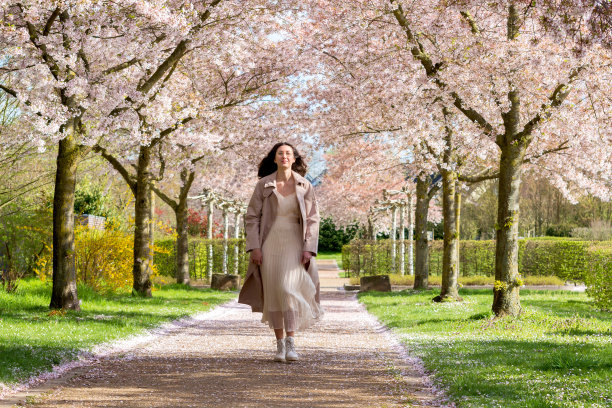一个年轻女孩的肖像，她穿着漂亮的裙子，背景是色彩柔和的樱花，她沿着小巷走着。女人的自然美。春天的概念。图片下载