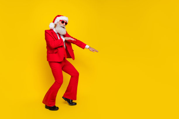 有吸引力的正面圣诞老人穿着红色的衣服跳舞，有乐趣的迪斯科舞厅空的空间孤立的黄色背景的全身照片图片下载