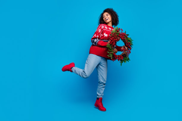 照片中的快乐开朗的女孩穿着时髦的印花毛衣，看起来空的空间常绿花环孤立的蓝色背景图片下载