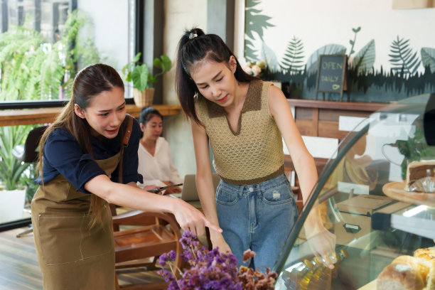 穿着围裙的年轻女店主正在介绍蛋糕菜单，并拿着平板电脑接受在玻璃柜里挑选蛋糕的顾客的点餐图片下载