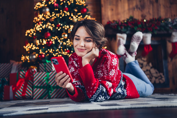 可爱宁静的女孩的全尺寸照片铺设地板使用智能手机新年树灯装饰礼盒平面室内图片下载