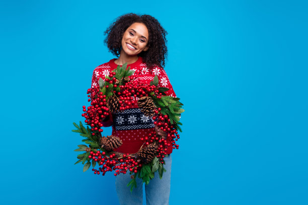 可爱可爱的女孩的照片穿着时髦的装饰套头衫抱着云杉花环装饰家空旷的空间孤立的蓝色背景图片下载