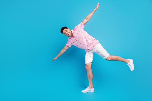 积极疯狂的人的全身照片，站着一条腿，双手翅膀空的空间孤立在蓝色的背景图片下载