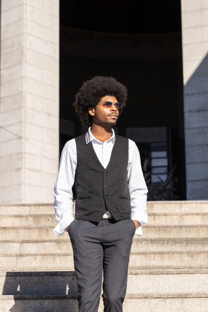 一个戴着墨镜，卷发的黑人男孩在婚礼后离开教堂。垂直图图片下载