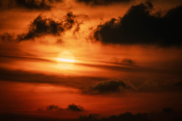 风景优美的橘红色日落，太阳隐藏在云层中，发光的光线线水平穿过太阳盘，特写照片。泰国图片下载