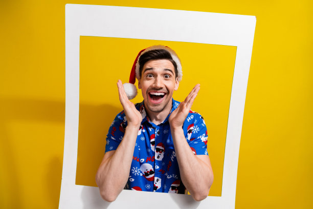 年轻的圣诞老人庆祝概念性聚会的照片，纸框架边界区域令人惊讶的双手脸颊孤立在黄色背景上图片下载