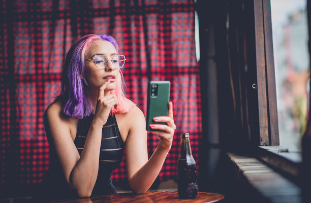 一名年轻女子坐在长凳上玩手机的照片。图片下载