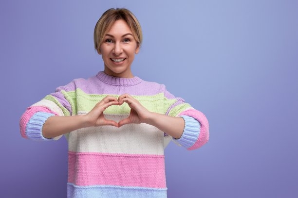 微笑的金发年轻女子在紫色的背景上展示了她的心图片下载