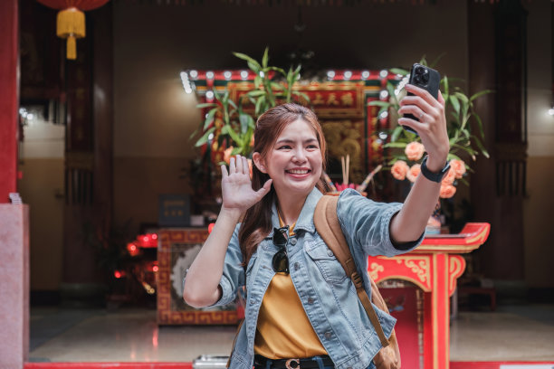 身穿蓝色夹克的年轻亚洲女子用相机或手机在中国寺庙拍摄欢快的照片或自拍。图片下载