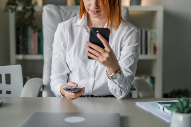 一位女企业家手持手机和遥控器在办公室调节空调，运用科技理念图片下载
