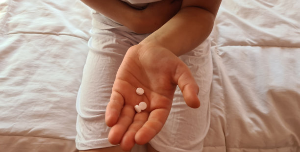 肚子痛的孩子躺在床上，手里拿着药图片下载