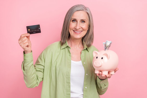 照片积极成功的养老金领取者穿着时髦的衣服拿着猪盒塑料卡无现金支付孤立在粉红色的背景图片下载
