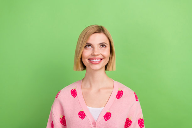 年轻迷人的女士穿着粉红色时髦迷人的开襟羊毛衫的照片抬头看感兴趣的想象周末孤立在绿色的背景图片下载
