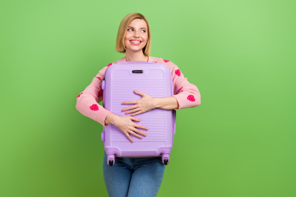 照片中迷人的年轻女子行李箱看起来空荡荡，穿着时髦的粉红色草莓印花衣服，孤立在绿色背景上图片下载