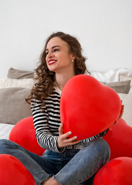 一个快乐微笑的年轻女子手持情人节气球的垂直照片图片下载