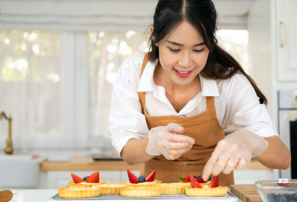 快乐的年轻家庭主妇手戴烹饪手套，用蓝莓草莓新鲜水果装饰新鲜出炉的馅饼。女厨师面包师戴着围裙做水果馅饼。在家自制面包店。图片下载