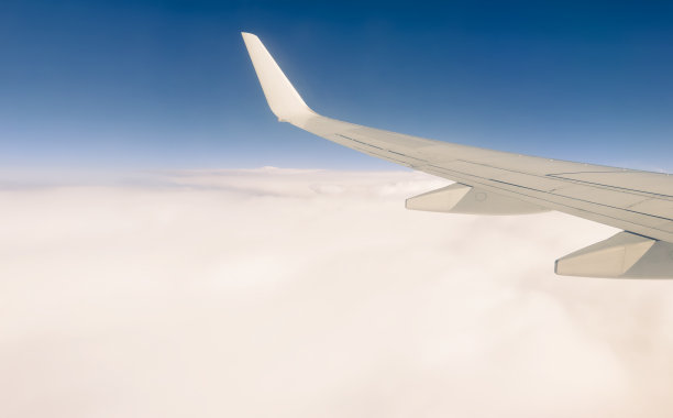 阳光明媚的日子里，飞机窗外的白色翅膀。风景非常好。从飞机窗口鸟瞰云层。飞机的机翼上有蓝天和美丽的云图片下载
