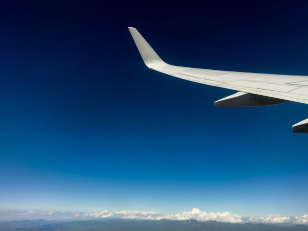 阳光明媚的日子里，飞机窗外的白色翅膀。风景非常好。从飞机窗口鸟瞰云层。飞机的机翼上有蓝天和美丽的云图片下载