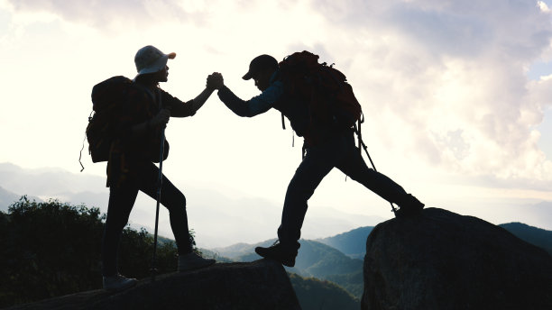 一对情侣背着背包，拄着登山杖，合作，在黄昏的天空下，在山上徒步旅行。旅行的概念。图片下载