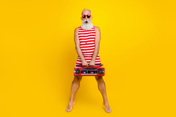疯狂的游客的全身照片惊讶的退休老人保持踮起脚尖拿着时髦的立体声音箱孤立的黄色背景图片下载