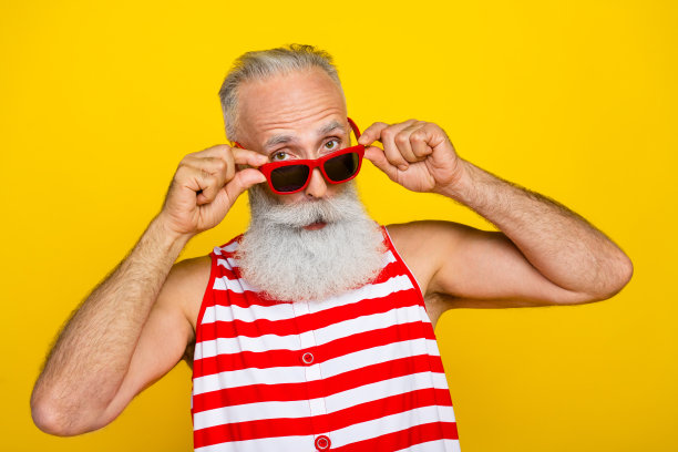 照片上开朗多疑的老年男子身穿红色条纹泳衣，双手手臂戴着墨镜望着你空旷孤立的黄色背景图片下载