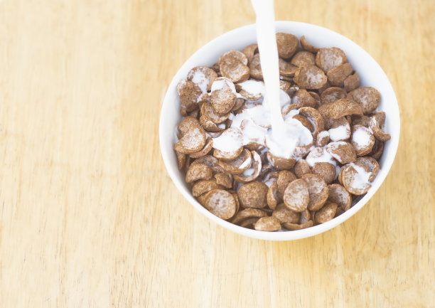 图片俯视图将牛奶倒在谷物巧克力上，在碗里用玉米制成，白色是一种食物早餐，木桌背景为文字的复制空间。图片下载