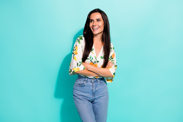 漂亮女人的照片，长发，穿着印花衬衫，双手折叠，在绿松石色的背景上看起来空空荡荡图片下载