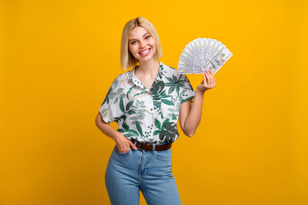 漂亮的年轻女孩的照片肖像，拿着钞票，扇钱，穿着时尚的树叶印花服装，孤立在黄色背景上图片下载