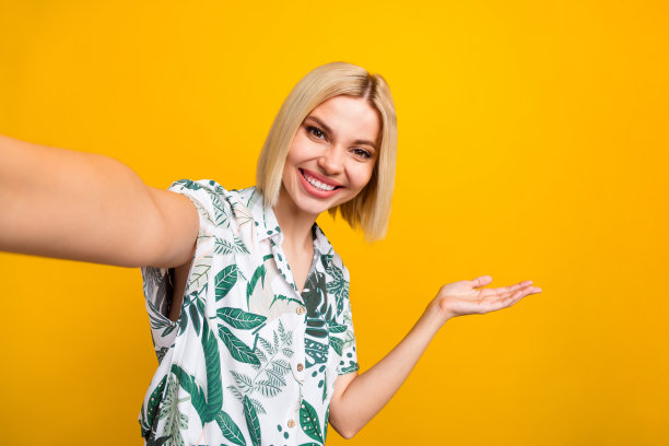照片肖像迷人的年轻女子自拍持有空白空间穿着时尚的树叶印花衣服孤立在黄色背景图片下载