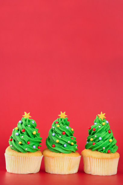 图片一排三，自制的，圣诞树设计的纸杯蛋糕，绿色的奶油漩涡装饰着五颜六色的糖屑，红色的背景，重点在前景，复制空间图片下载