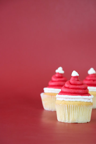 图片批三，自制，圣诞老人帽子设计纸杯蛋糕，红色奶油漩涡装饰白色糖衣球，红色背景，重点在前景，复制空间图片下载